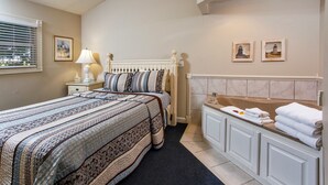Un dormitorio con una cama grande, una mesita de noche, una lámpara, una ventana con persianas y un baño con bañera y toallas.