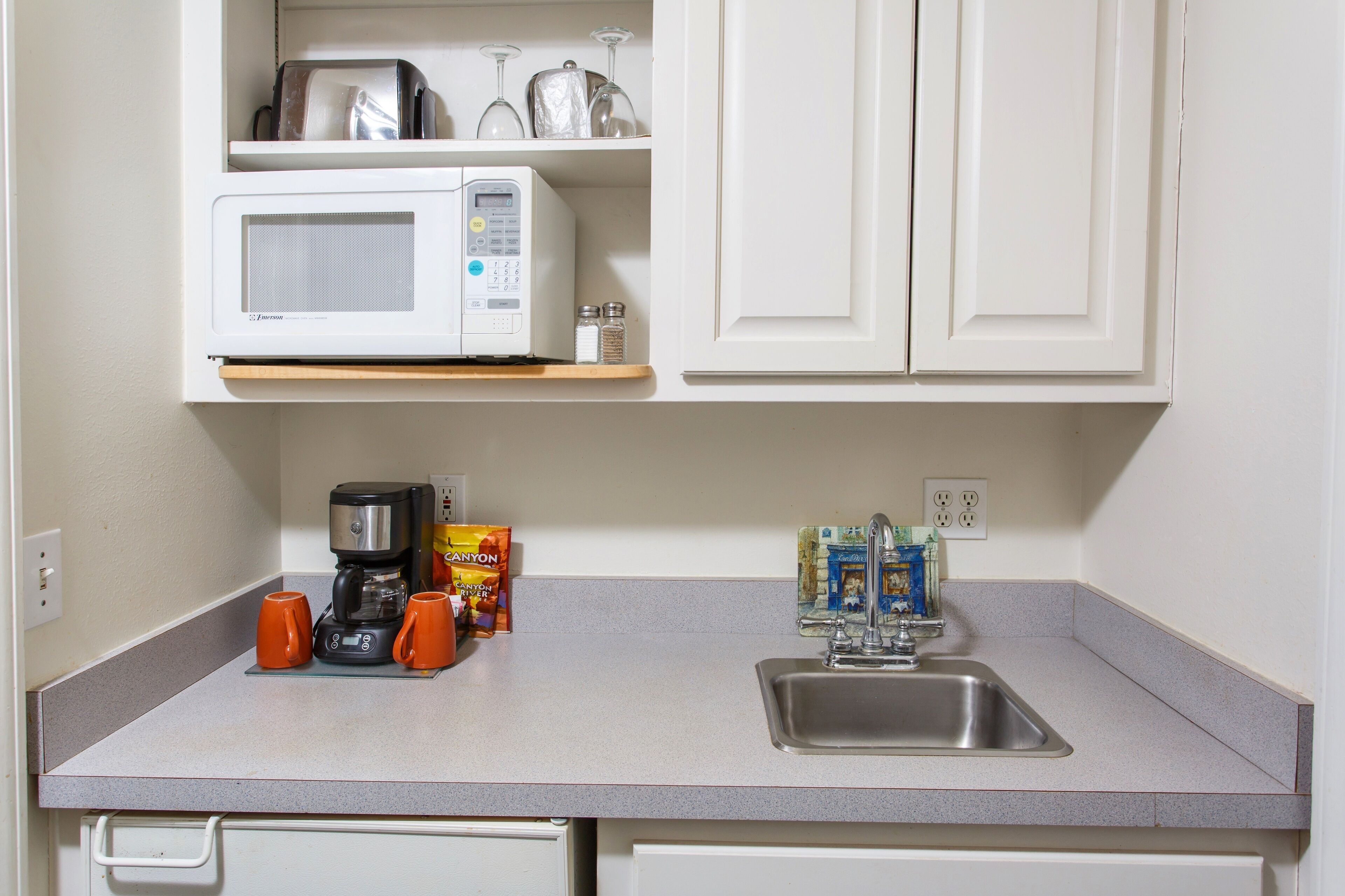 Een kitchenette met een magnetron, koffiezetapparaat en zout- en peperstel op het aanrecht.