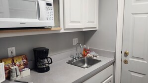 Una cocina con microondas, cafetera, lavamanos y armarios.