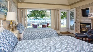 Una habitación de hotel con dos camas, chimenea, televisor y vista a un puerto deportivo.