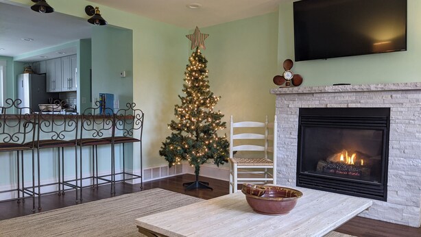 A living room with a fireplace, a Christmas tree, and a dining table. - Beach Harbor Resort - Deluxe Apartment (Sturgeon Bay)