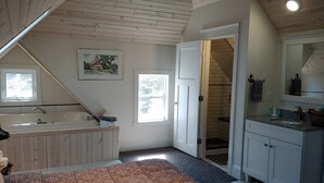A bedroom with a large bed, a window, a bathroom with a bathtub, and a shower. - Beach Harbor Resort - Deluxe Apartment (Sturgeon Bay)