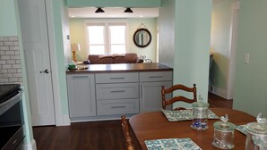 A dining area with a wooden table, chairs, and a kitchen in the background. - Beach Harbor Resort - Deluxe Apartment (Sturgeon Bay)