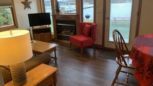 A cozy living room with a fireplace, a television, and a view of a body of water. - Snug Harbor Inn - 2 Bedroom Cottage (Sturgeon Bay)