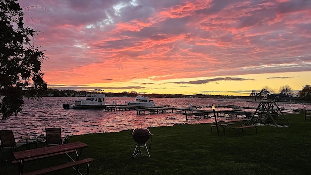 A lakeside view with boats docked, picnic tables, and a grill. - Snug Harbor Inn - 2 Bedroom Cottage (Sturgeon Bay)