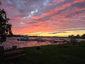 A lakeside view with boats docked, picnic tables, and a grill.