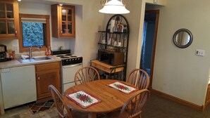 A compact kitchen with a stove, sink, and microwave. There is a dining table with chairs and a Christmas-themed placemat. - Snug Harbor Inn - Luxury Cottage 4 (Sturgeon Bay)