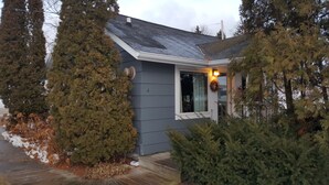 A small house with a grey exterior, a white door, and a lit window. - Snug Harbor Inn - Luxury Cottage 4 (Sturgeon Bay)