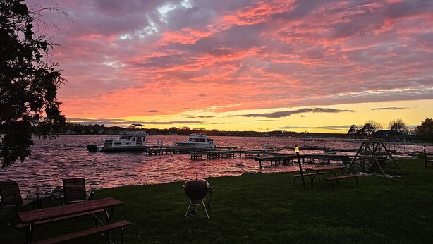 A lakeside view with boats docked, picnic tables, and a grill. - Snug Harbor Inn - Luxury Cottage 4 (Sturgeon Bay)