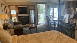 A hotel room with a large bed, a sofa, a TV, a fireplace, a dining area with chairs, and a kitchen area. - Snug Harbor Inn - Luxury Cottage 4 (Sturgeon Bay)