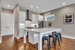 Une cuisine moderne avec des meubles blancs, un îlot central doté de tabourets et des luminaires suspendus.