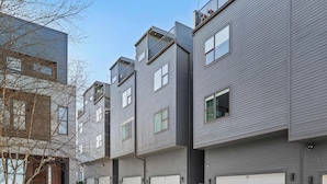 A row of modern multi-story residential buildings with grey siding, multiple garage doors, and a clear sky.