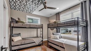 A room with two bunk beds, a ceiling fan, a window with curtains, and a patterned rug.