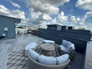 Eine Dachterrasse mit Gartenmöbeln und Blick auf die Stadt, der Himmel ist wolkenlos.