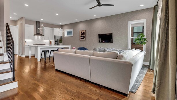 Ein modernes Wohnzimmer mit einem großen, beigefarbenen Ecksofa, einem Essbereich mit einer weißen Kochinsel und einer Küche im Hintergrund.