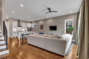 A modern living room with a large beige sectional sofa, a dining area with a white island, and a kitchen in the background.