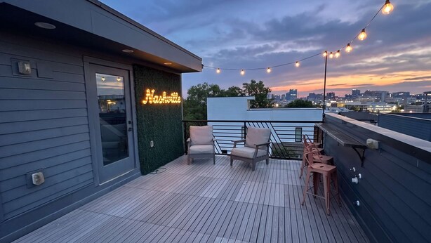 A rooftop terrace with a seating area, string lights, and a city skyline view.