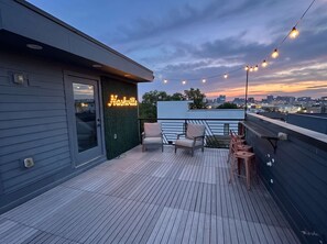 Une terrasse sur le toit, dotée d’un espace salon, de guirlandes lumineuses et offrant une vue panoramique sur la ville.