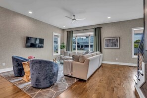 Un salon spacieux comprenant un grand canapé, deux fauteuils, un téléviseur à écran plat et un ventilateur de plafond.