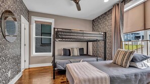 Ein Zimmer mit Etagenbett, einem Einzelbett, einem Deckenventilator, einem Fenster mit Vorhängen und ornamentalem Wandpapier.