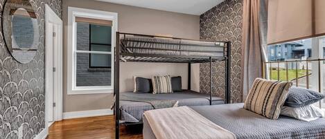 Ein Zimmer mit Etagenbett, einem Einzelbett, einem Deckenventilator, einem Fenster mit Vorhängen und ornamentalem Wandpapier.