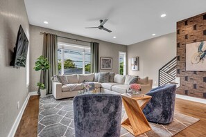 Un salon moderne comprenant un canapé d’angle, deux fauteuils, une table basse et un ventilateur de plafond.