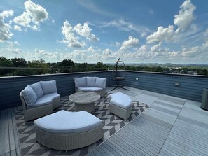 A rooftop patio with wicker furniture, a hanging chair, and a patterned rug.
