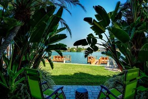 A view of a pool area with wooden deck chairs and a grassy lawn, surrounded by tropical plants. - Treasure Island, Florida             Waterfront Resort (Treasure Island)