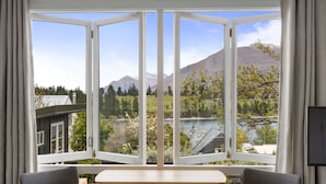 A room with a large window offering a view of a lake, mountains, and a building across the water. - Stay of Queenstown (Queenstown)