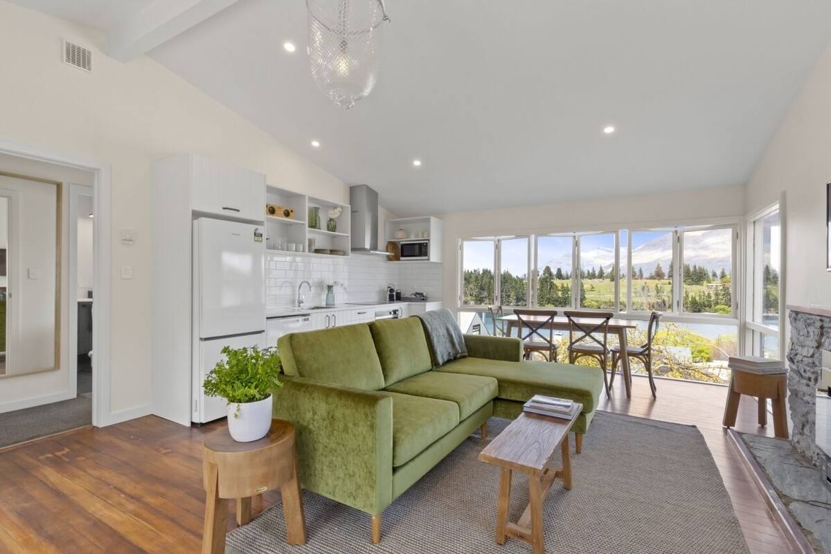 A modern kitchen with white appliances, a green sofa, and a dining area with a view of the outdoors.