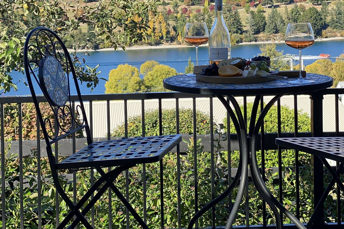 A balcony with a table set for a meal, overlooking a lake and mountains.