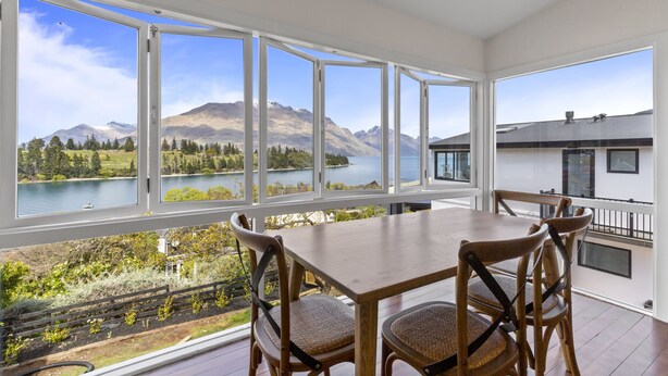 A dining area with a table and chairs, large windows offering a view of mountains and a lake. - Stay of Queenstown (Queenstown)