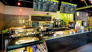 Una cafetería con un mostrador que exhibe pasteles y una sección refrigerada con bebidas.