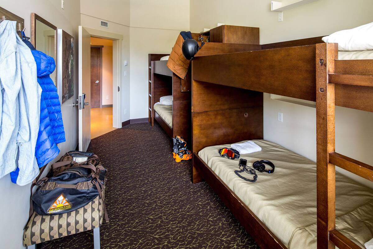 Ein Hotelzimmer mit Etagenbetten, einem Koffer, einer Mütze und einer Schutzbrille auf dem Bett.