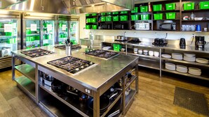 Una cocina comercial con electrodomésticos de acero inoxidable, contenedores de almacenamiento verdes y una alacena para alimentos.