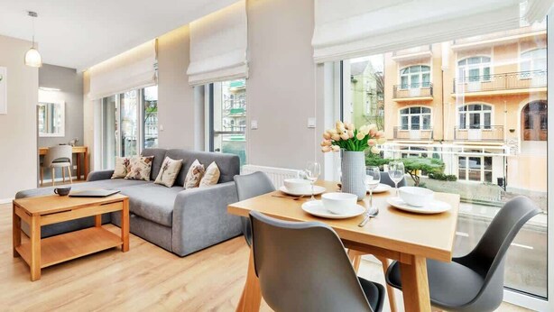 A modern living room with a sofa, dining table, and chairs, a small wooden table, and a vase with flowers. - Modern Apartment | Balcony, Parking, Workspace (Swinoujscie)