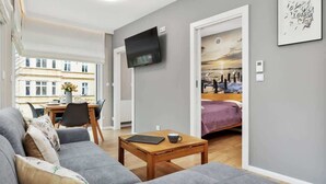 A modern living room with a sofa, a coffee table, a TV mounted on the wall, and a bed with a painting. - Modern Apartment | Balcony, Parking, Workspace (Swinoujscie)