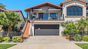 A two-story house with a garage, a balcony, and a staircase leading to the second floor. - Coastal Modern Beach Cottage-2 Bed/2 Bath, A/C, Vegetable Garden, Walk2Beach (Dana Point)