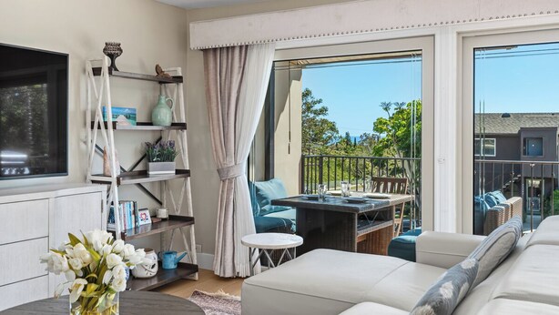 A living room with a sofa, a TV, a bookshelf, and a balcony with outdoor furniture. - Coastal Modern Beach Cottage-2 Bed/2 Bath, A/C, Vegetable Garden, Walk2Beach (Dana Point)