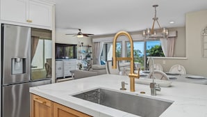 A modern kitchen with a stainless steel refrigerator, a white marble countertop, a gold faucet, and a ceiling fan. - Coastal Modern Beach Cottage-2 Bed/2 Bath, A/C, Vegetable Garden, Walk2Beach (Dana Point)