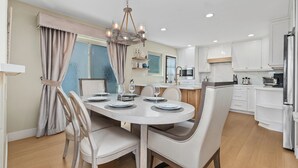 A modern kitchen with white cabinets, a dining area with a round table and chairs, and a chandelier. - Coastal Modern Beach Cottage-2 Bed/2 Bath, A/C, Vegetable Garden, Walk2Beach (Dana Point)