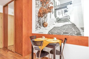 Un comedor con una mesa dispuesta para dos, piso de madera y un cuadro colgado en la pared que muestra una escena callejera.