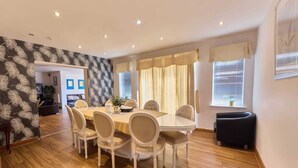 Un comedor con una mesa redonda y seis sillas, una sala de estar con un sofá y una mesa de centro, y una cocina con estufa y alacenas.