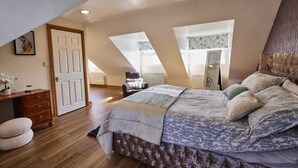 Un dormitorio con una cama grande, un escritorio y una silla. Hay tragaluces y una puerta.