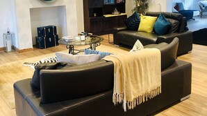Un amplio salón con un gran sofá de cuero negro, una mesa de centro de vidrio y una estantería.