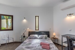 A modern hotel room with a bed, a desk, a chair, a lamp, and a framed picture on the wall.