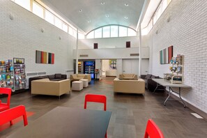 A spacious lobby with high ceilings, white brick walls, and a variety of seating arrangements including sofas and chairs.