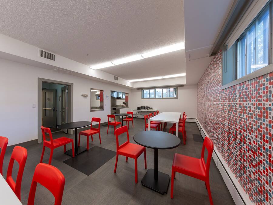 A conference room with red chairs and tables, a kitchenette, and a patterned wall.