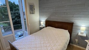 Quarto com cama de madeira, uma janela grande e luminária fixada na parede.