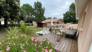 Eine Holzterrasse mit Gartenmöbeln, umgeben von Grünpflanzen und blühenden Blumen.
